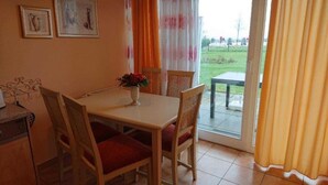 Un comedor con una mesa y sillas, un florero con flores, y vista al exterior a través de un ventanal.