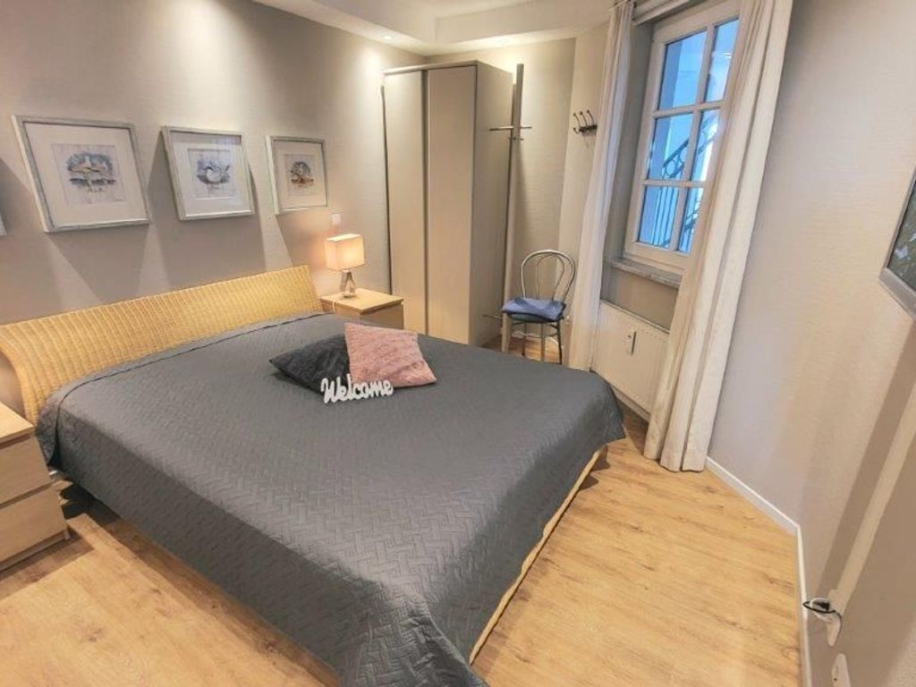 A bedroom with a bed, a nightstand, a chair, a window, and framed pictures on the wall.