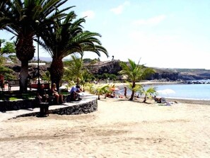 Ein Strand mit Palmen, einem Felsen und blauem Himmel.