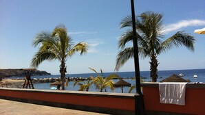 Vista de playa con palmeras, una cabaña de techo de paja y un cielo azul despejado.