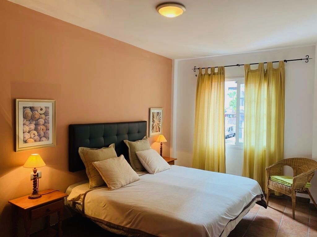 A hotel room with a bed, two bedside lamps, a chair, and a window with curtains.
