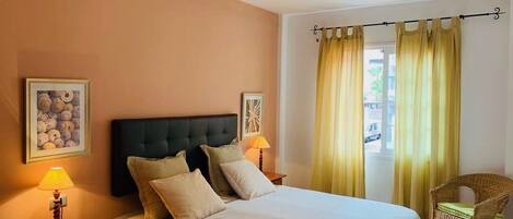 A hotel room with a bed, two bedside lamps, a chair, and a window with curtains.