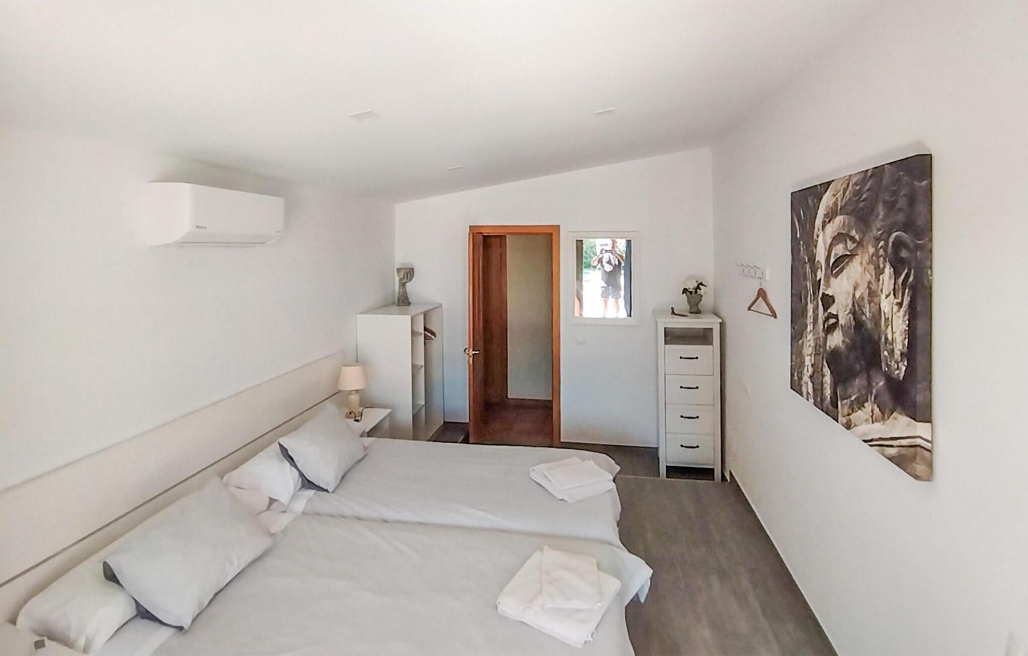 Un dormitorio con una cama grande, una mesita de noche con lámpara, un armario y un cuadro en la pared.