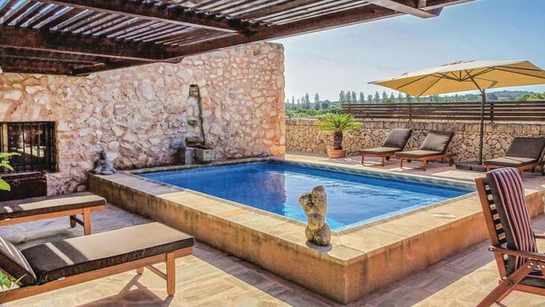 Una piscina con paredes de piedra, sillones de descanso y una pérgola.