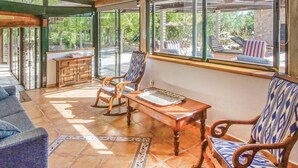 Habitación iluminada por el sol con vistas al exterior, que incluye una mesa de madera, dos mecedoras y un sofá.