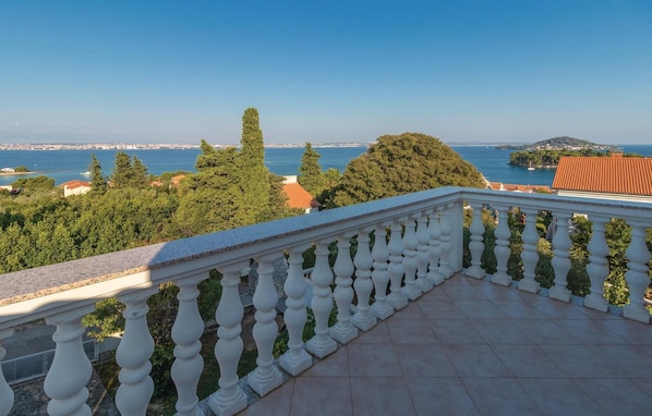 Ein Balkon mit weißer Brüstung, der auf eine Küstenlandschaft mit Bäumen und Blick aufs Meer blickt.