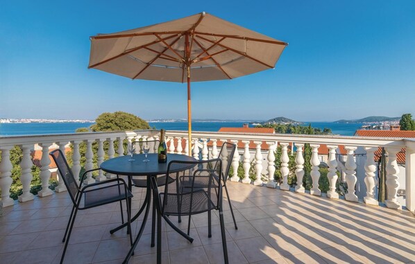 A balcony with a table and chairs, a beige umbrella, and a view of the sea and distant buildings. - 4 bedroom stunning apartment in Poljana (Poljana)