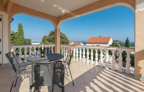A covered outdoor seating area with a table and chairs, overlooking a coastal view with buildings and trees. - 4 bedroom stunning apartment in Poljana (Poljana)