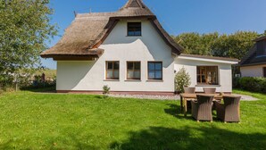 A house with a thatched roof, white walls, and a small garden with a table and chairs. - Thatched Cottage in Dierhagen - Thatched Cottage (1) (Dierhagen)