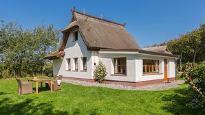 A traditional house with a sloped roof, a small porch, and a garden area with a table and chairs. - Thatched Cottage in Dierhagen - Thatched Cottage (1) (Dierhagen)