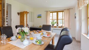 A dining area with a wooden table set for breakfast, including plates of food, cups, and a vase of flowers. - Thatched Cottage in Dierhagen - Thatched Cottage (1) (Dierhagen)