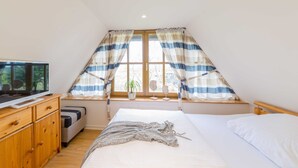 A bedroom with a bed, a wooden dresser, a television, and a window with curtains. - Thatched Cottage in Dierhagen - Thatched Cottage (1) (Dierhagen)