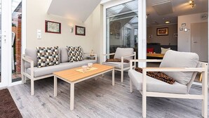 A modern living room with a sofa, chairs, and a coffee table. There is a sliding glass door leading to a kitchen area. - Holiday house Watt'n Huus (Dornum)