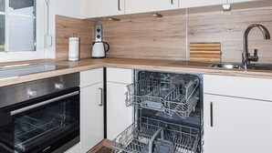 A modern kitchen with white cabinets, a wooden countertop, a built-in dishwasher, and a coffee maker. - Holiday house Watt'n Huus (Dornum)