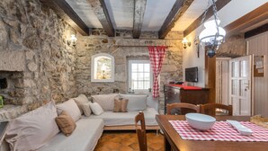 A cozy room with a stone wall, a wooden ceiling, a sofa with cushions, a dining table with a bowl, and a television on the wall. - Lovely home in Crikvenica with WiFi (Crikvenica)