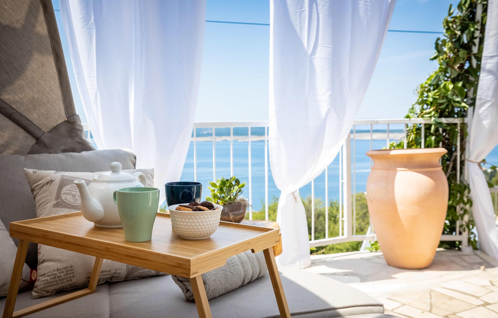 Ein Balkon mit Tisch, der für Tee gedeckt ist, einer Topfpflanze und einem großen Terrakottatopf.