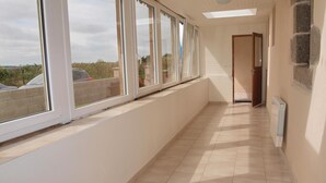 Un passadís llarg i estret amb grans finestres a un costat, que condueix a una porta al final.