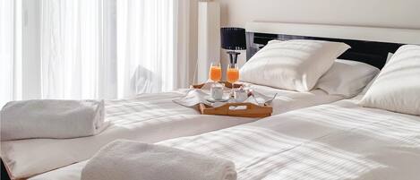 Habitación de hotel con una cama bien hecha, dos toallas, una bandeja con dos vasos de jugo de naranja y una taza de café.