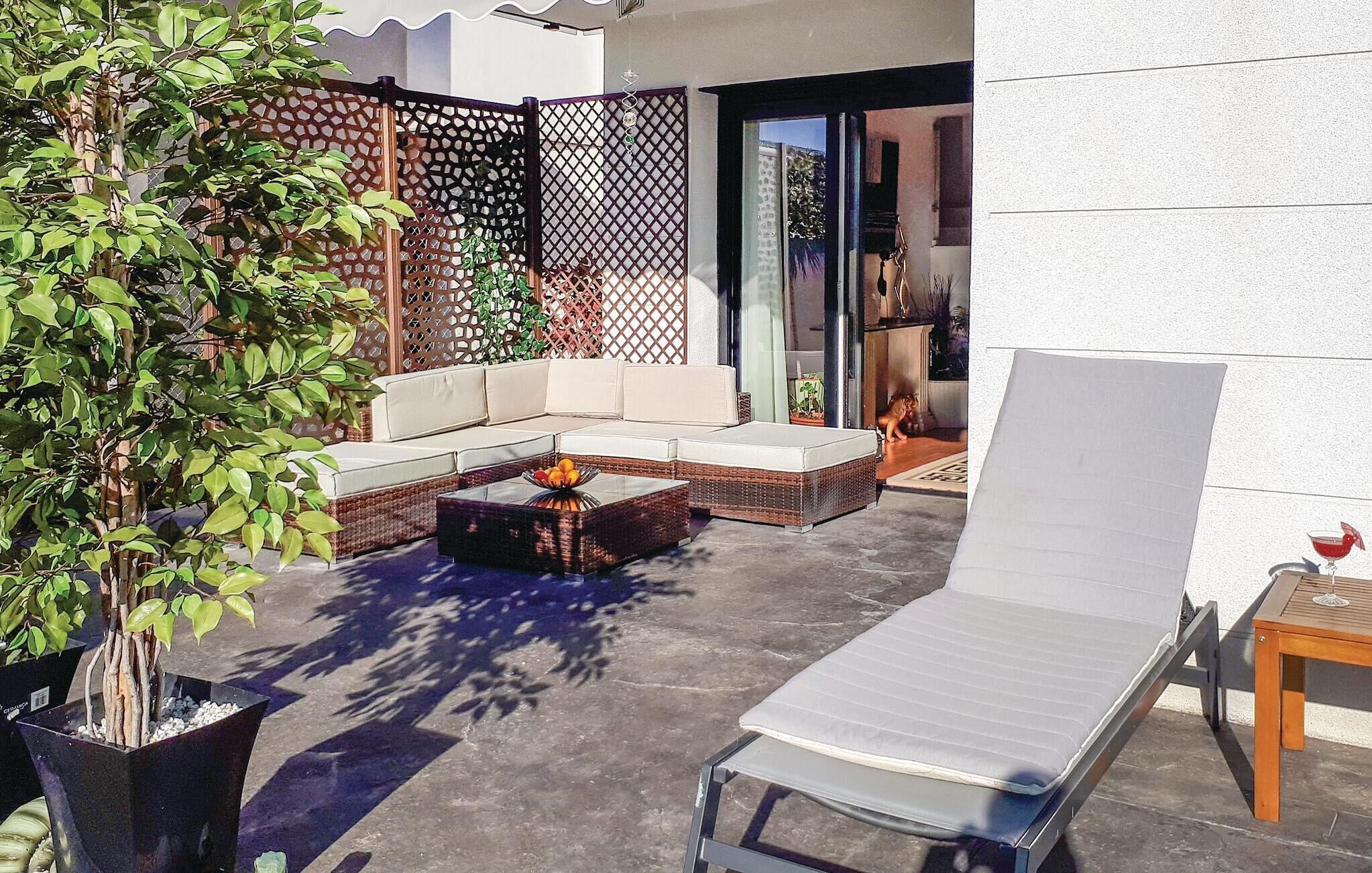 An outdoor patio area with a sofa, a coffee table, a lounge chair, and a potted plant.