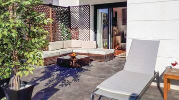 An outdoor patio area with a sofa, a coffee table, a lounge chair, and a potted plant.