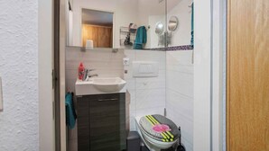 Une petite salle de bain avec un lavabo blanc, un miroir et des toilettes.
