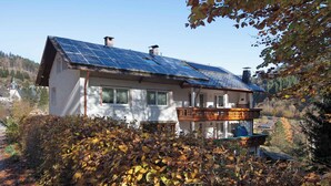 Une maison dotée d’un toit recouvert de panneaux solaires, d’un balcon et offrant une vue sur une zone boisée.