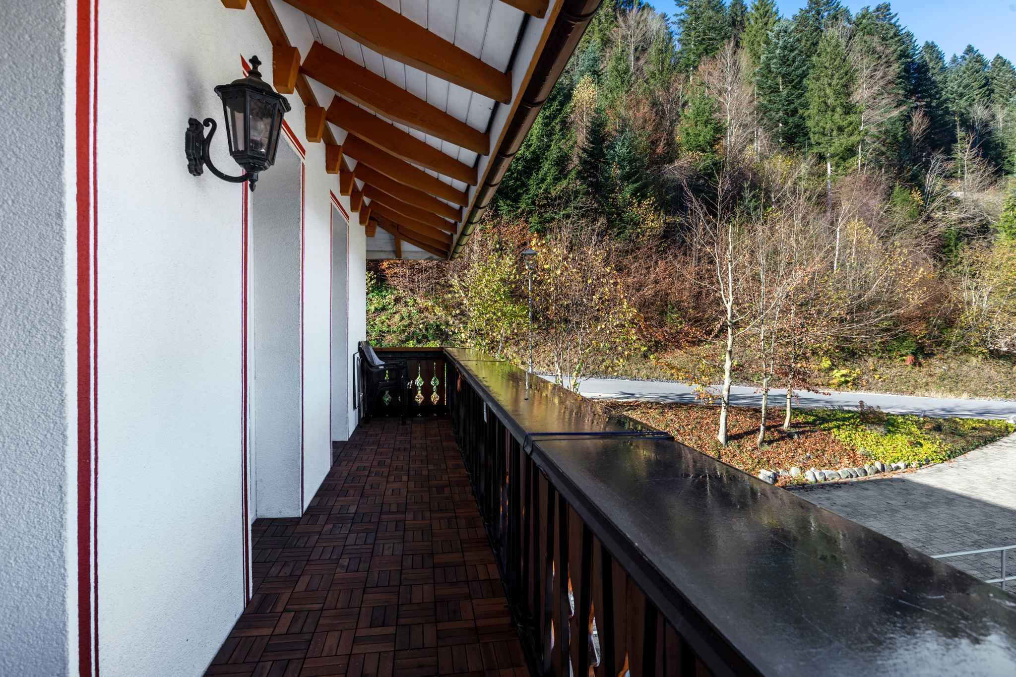 A covered outdoor area with a brick floor, wooden beams, and a railing overlooking a forested landscape.