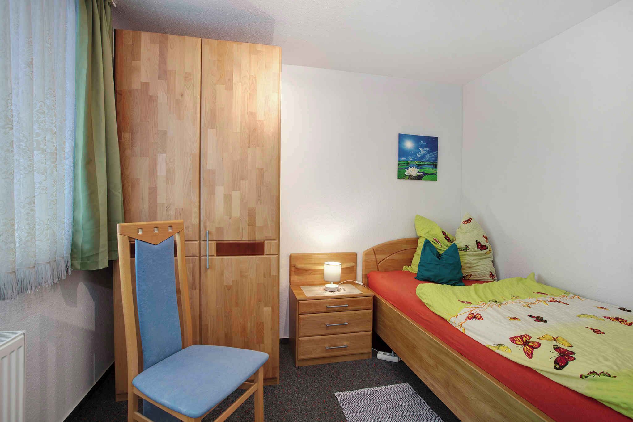 A bedroom with a bed, a chair, a wardrobe, a nightstand, and a wall-mounted painting.