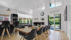 Une cuisine spacieuse avec une table à manger en bois, des chaises noires et une grande fenêtre donnant sur un espace verdoyant.