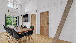 Une pièce spacieuse avec une longue table en bois et des chaises noires, des murs blancs et une grande fenêtre.