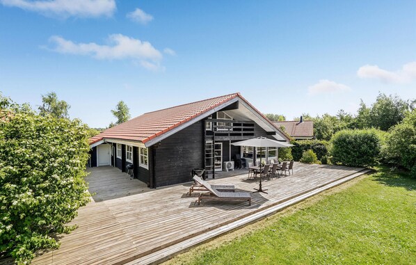 Et moderne hus med en stor terrasse, et overdækket udendørs opholdsområde og et rødt tegltag.