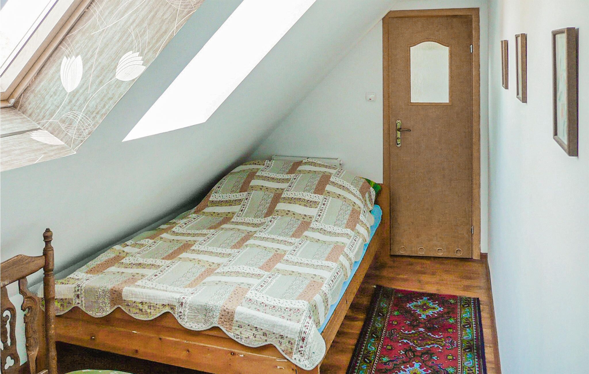 A small, cozy room with a wooden bed, a door, and a window with a view of the sky.