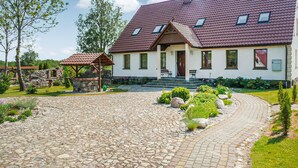 A house with a stone driveway, a wooden pergola, and a garden with rocks and plants. - Nice home in Pl-76-113 Postomino (Pl-76-113 Postomino)