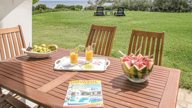 A wooden table set with a bowl of grapes, a tray with fruit and drinks, and a magazine titled 'NOVASOL'. - Soleiliosonne Haus Zeus (Ermioni)