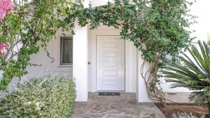 A stone-paved entrance with a white door, surrounded by lush greenery and a palm tree. - Soleiliosonne Haus Zeus (Ermioni)