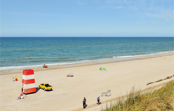 Ein Strand mit einem Rettungsturm, einem gelben Fahrzeug und Menschen, die am Ufer entlanggehen.