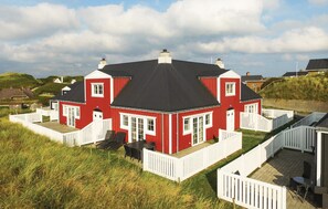 Ein zweistöckiges Haus in Rot und Weiß mit einem schwarzen Dach, umgeben von weißen Zäunen und Rasenflächen.