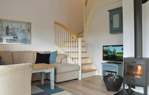 Ein Wohnzimmer mit Sofa, Tisch, Fernseher, Kamin und Treppe.