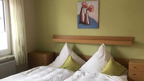 A bedroom with a wooden bed, white bedding, and a painting of flowers on the wall. - Vacation apartment (80 m²) - Gästehaus Müller (Walkenried)