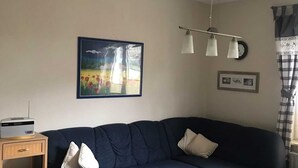 A living room with a dark blue sofa, a wooden coffee table with a sink, a lamp, and a painting on the wall. - Vacation apartment (80 m²) - Gästehaus Müller (Walkenried)