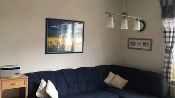 Ein Wohnzimmer mit einem dunkelblauen Sofa, einem Couchtisch aus Holz, einer Lampe und einem Bild an der Wand.