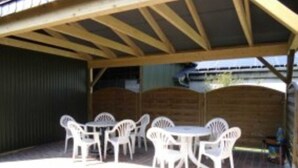 A covered patio area with a wooden ceiling and a brick floor. There are several white plastic chairs and a small round table. - Apartment 2 - Budach: Country vacation at the gates of Flensburg (Handewitt)