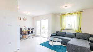 A modern living room with a grey sectional sofa, a glass coffee table, and a dining area with a wooden table and chairs. - Beautiful apartment in Valbandon (Valbandon)