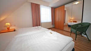 A hotel room with two beds, a wooden floor, a green chair, a window with curtains, and a mirror. - Haus Rügenwelle Whg. 04 1st floor with balcony/fireplace - W: Haus Rügenwelle with 4 (Baabe)
