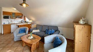 A cozy living area with a grey sofa, a wooden coffee table, and a kitchen in the background. - Haus Rügenwelle Whg. 04 1st floor with balcony/fireplace - W: Haus Rügenwelle with 4 (Baabe)