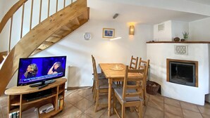 A living room with a wooden staircase, a dining table with chairs, a television, and a fireplace. - Haus Rügenwelle Whg. 04 1st floor with balcony/fireplace - W: Haus Rügenwelle with 4 (Baabe)
