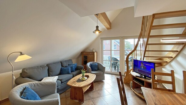 A cozy living room with a sofa, coffee table, and TV. There's a wooden staircase and a view of the outside. - Haus Rügenwelle Whg. 04 1st floor with balcony/fireplace - W: Haus Rügenwelle with 4 (Baabe)