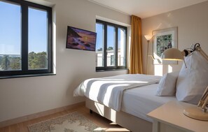 Un dormitorio con cama, ventana, un cuadro, lámpara y escritorio.