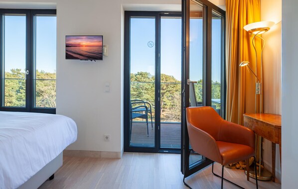 Un dormitorio con cama, una silla, un escritorio, un televisor y un balcón con vistas.
