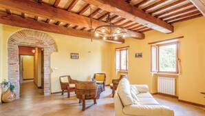 A spacious living room with a high wooden ceiling, a white sofa, and a dining area with wooden chairs and a barrel.